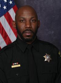 Deputy Ray Burns in law enforcement uniform in front of a grey background with an American flag