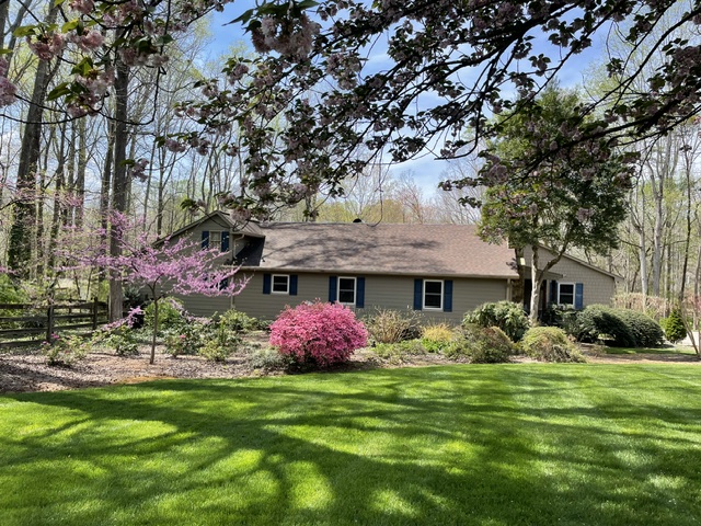 A tan home is surrounded by a lush island garden, leading to manicured green grass. Pops of purple and pink flowers add color to the beautiful landscape.