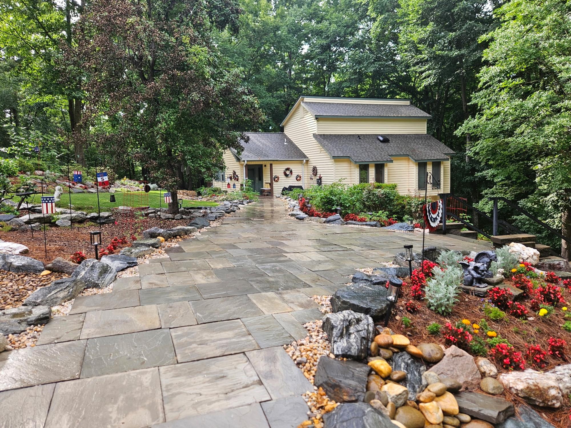 A beautiful outdoor pathway lined with large rocks and meticulously designed landscaping leads to a beautiful pale yellow home
