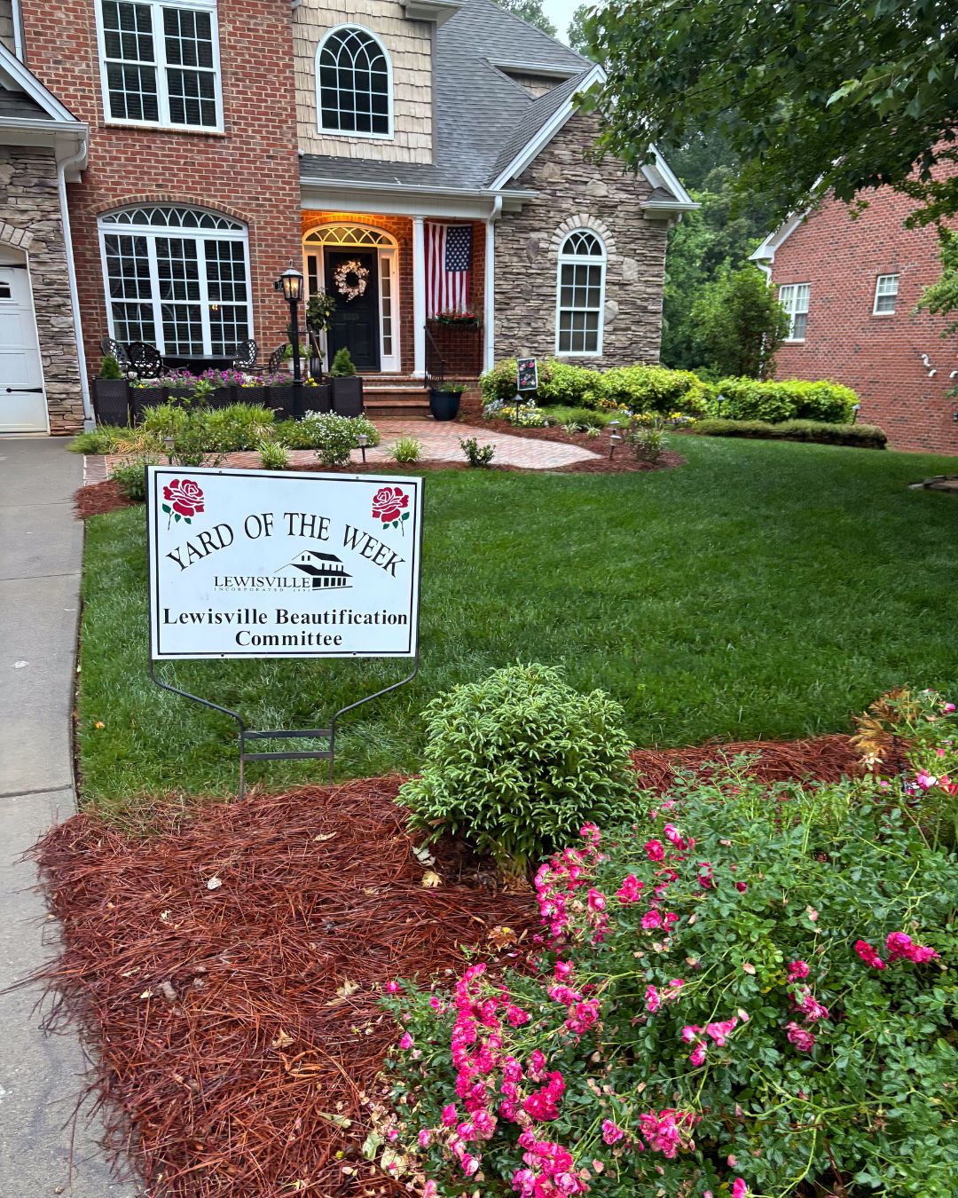 A beautiful home sits nestled in a lush lawn and pink flowers.