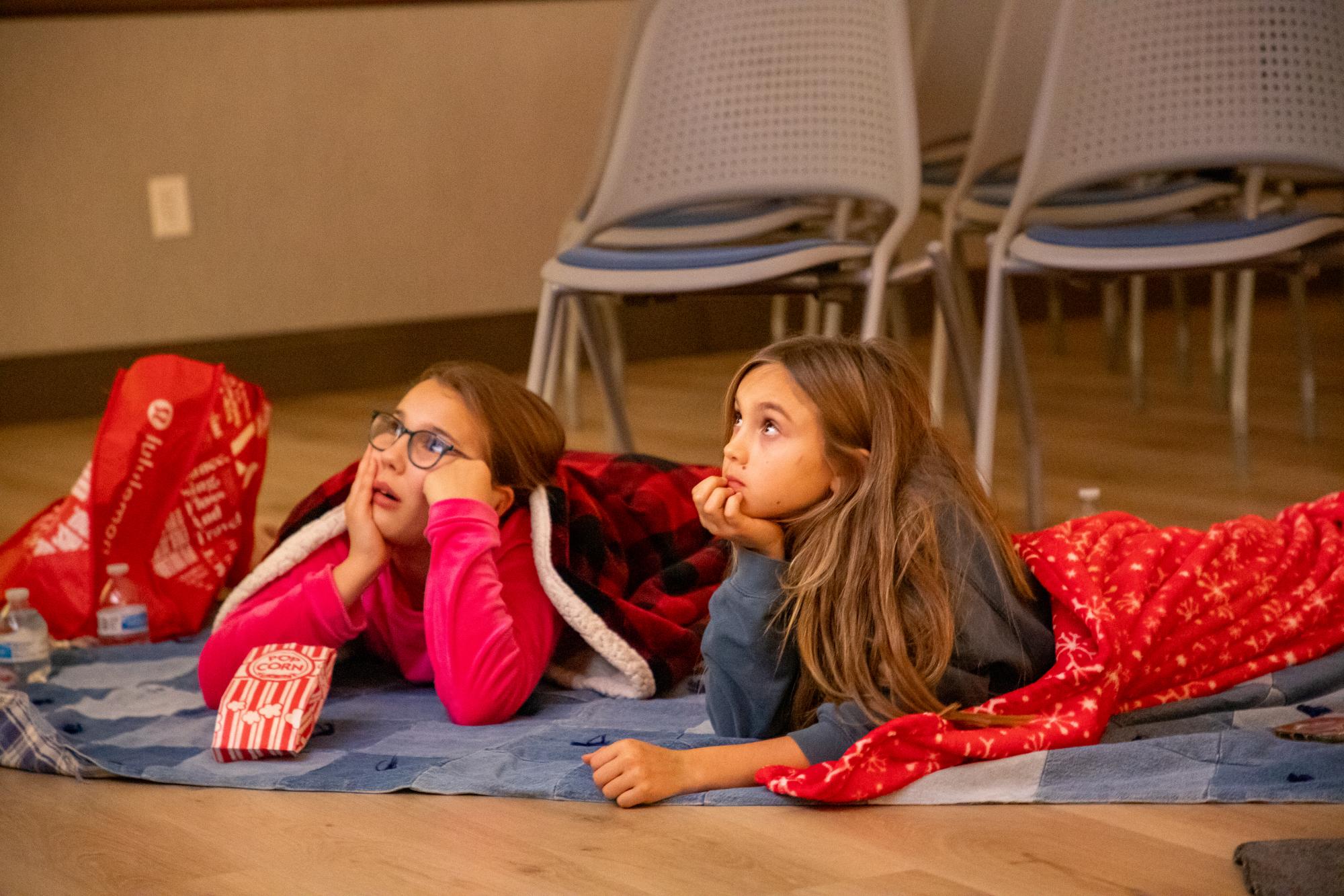 Two girls wrapped in sleeping bags watch a holiday movie at the Mary Alice Warren Community Center